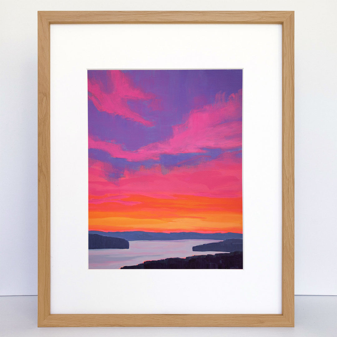 A framed vertical print showing a vibrant pink, orange, and purple sunset over a river.