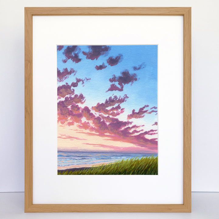 A framed print of colorful sunset over the beach. Dune grass in the foreground.