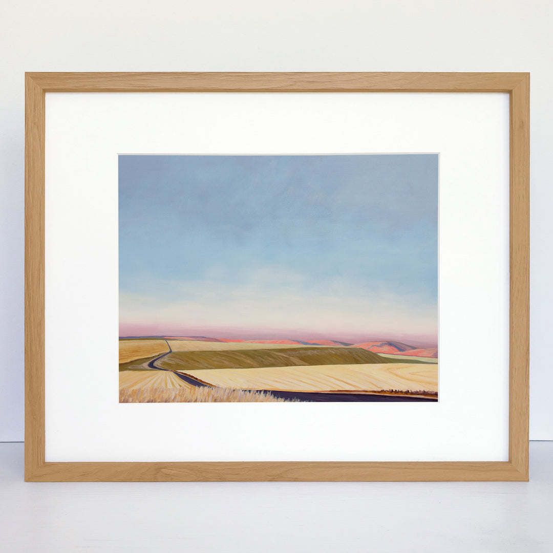 A framed horizontal art print showing rolling hills and an evening sky.