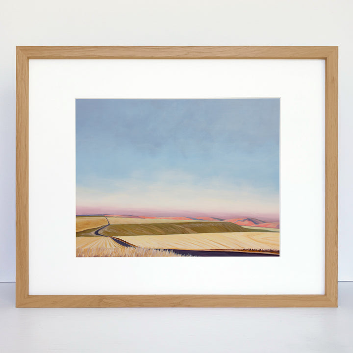 A framed horizontal art print showing rolling hills and an evening sky.
