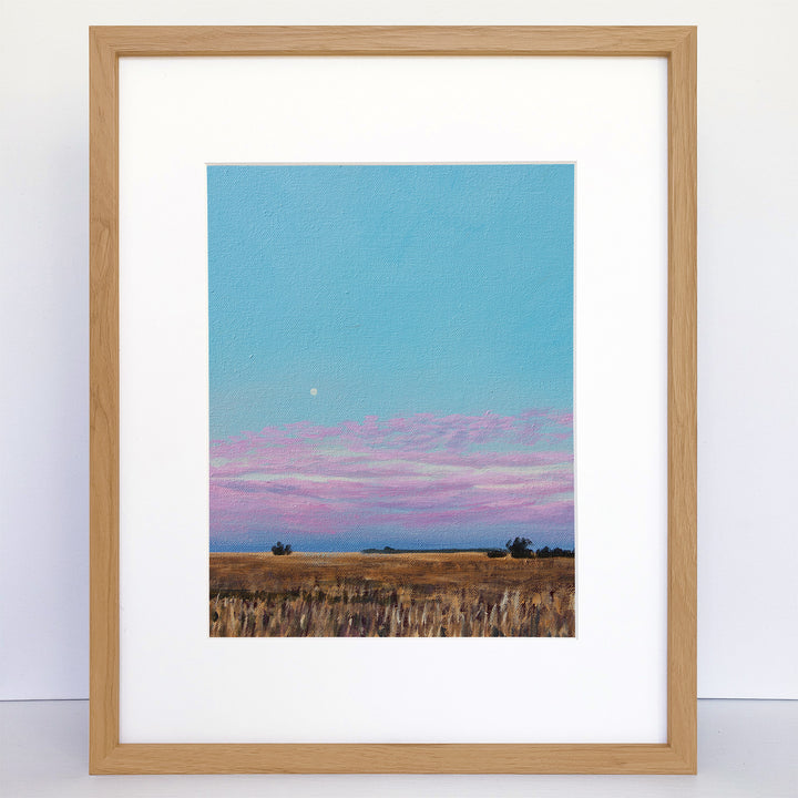 A framed art print showing the moon and pink clouds over a farm at dawn.