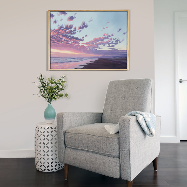 A room with a chair and a framed art print of a sunset over the ocean.