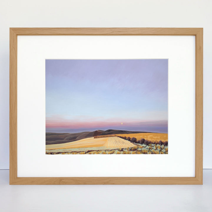 A framed contemporary art print with rolling hills, wheat fields, and a rising moon.