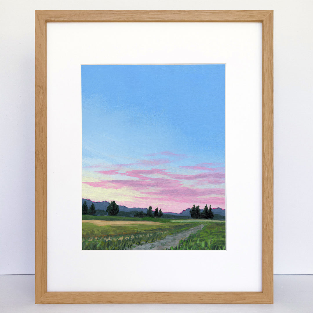A framed art print showing a dirt road with mountains in the distance and a sunset sky.