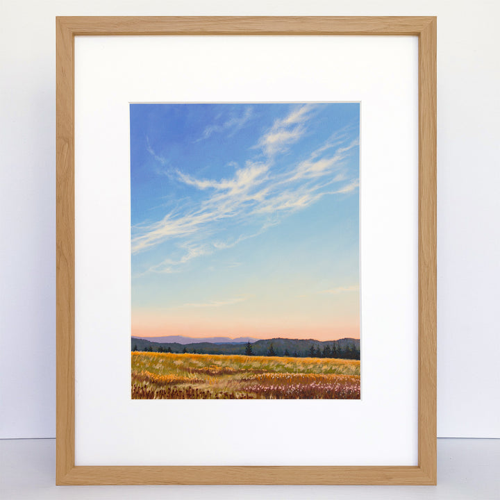 A framed art print of an evening sky with mountains in the distance and fields in the foreground.
