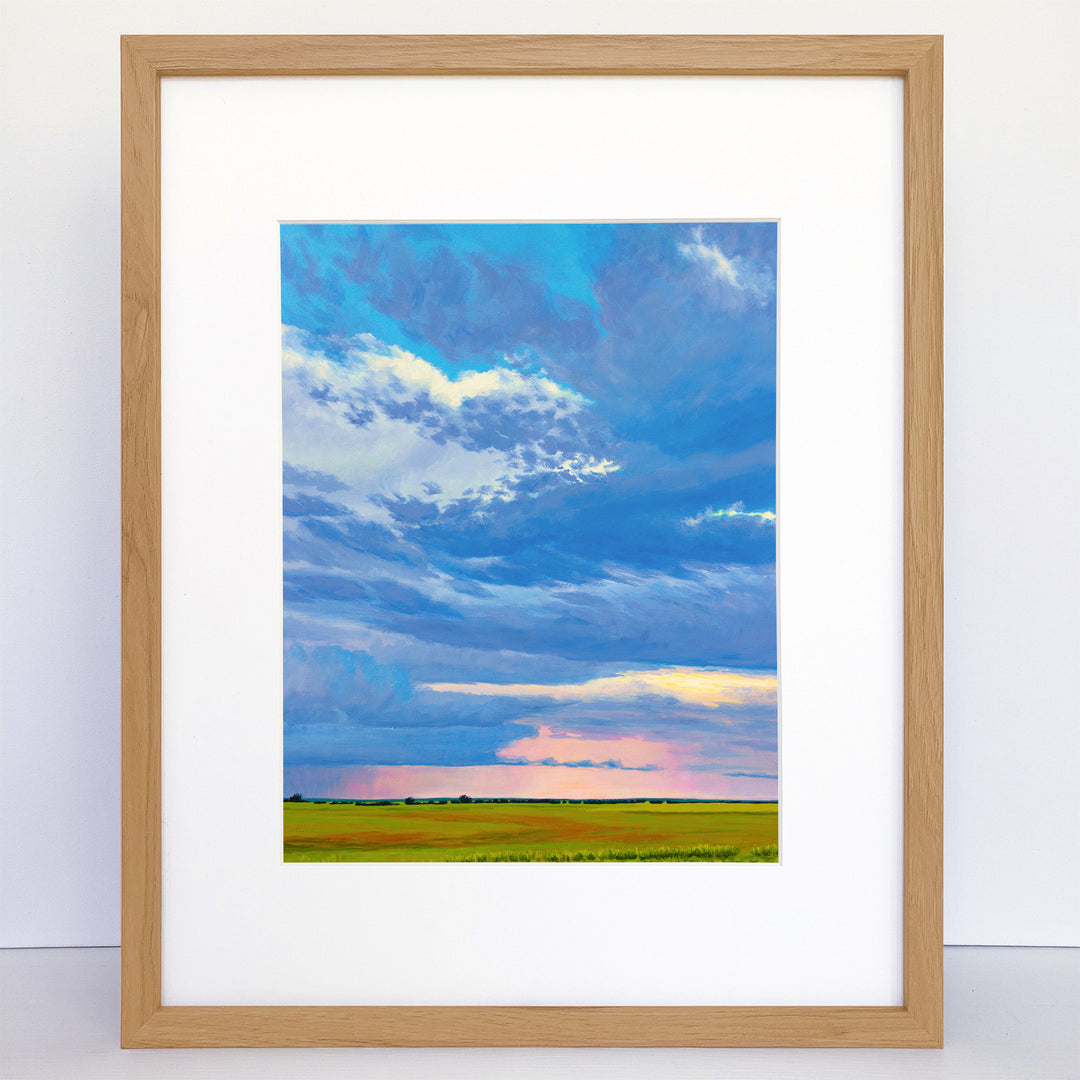 A framed art print of summer storm in the distance. Green fields, colorful sky.
