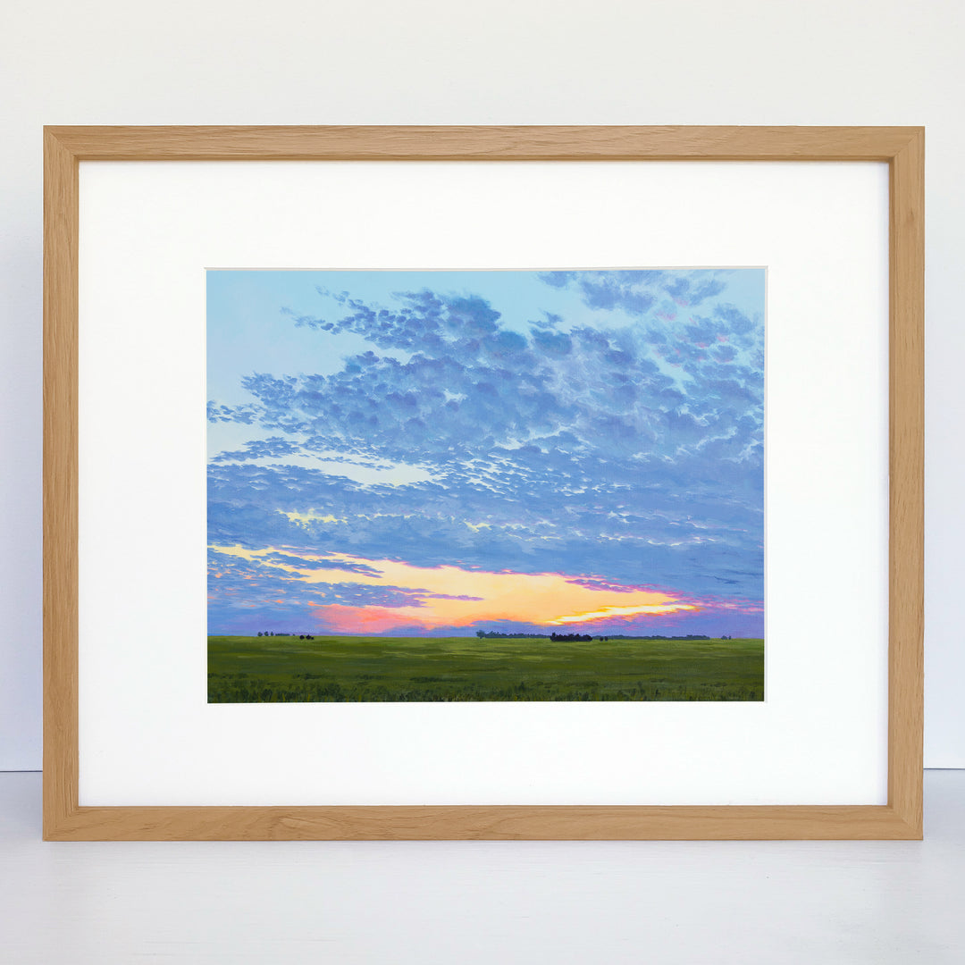A framed horizontal print of a colorful sunset over a green prairie.