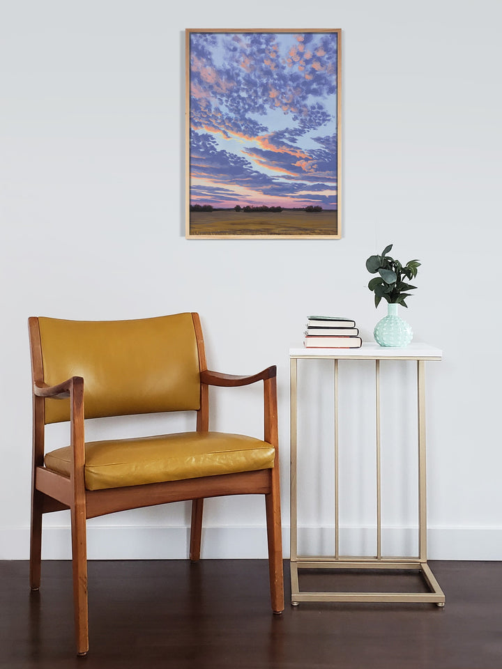 Framed wall art of a colorful sunset with a chair and side table.