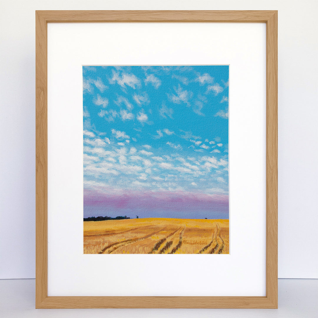 A framed vertical art print of freshly-cut wheat fields in the evening.